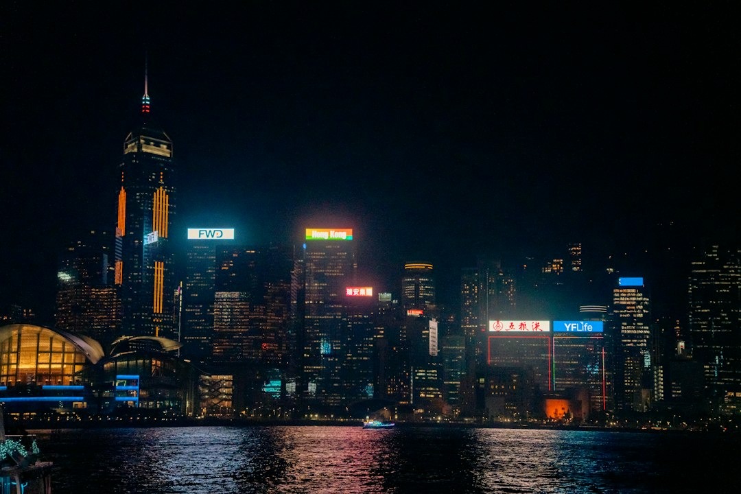 A small boat cruises past a brightly illuminated city skyline.